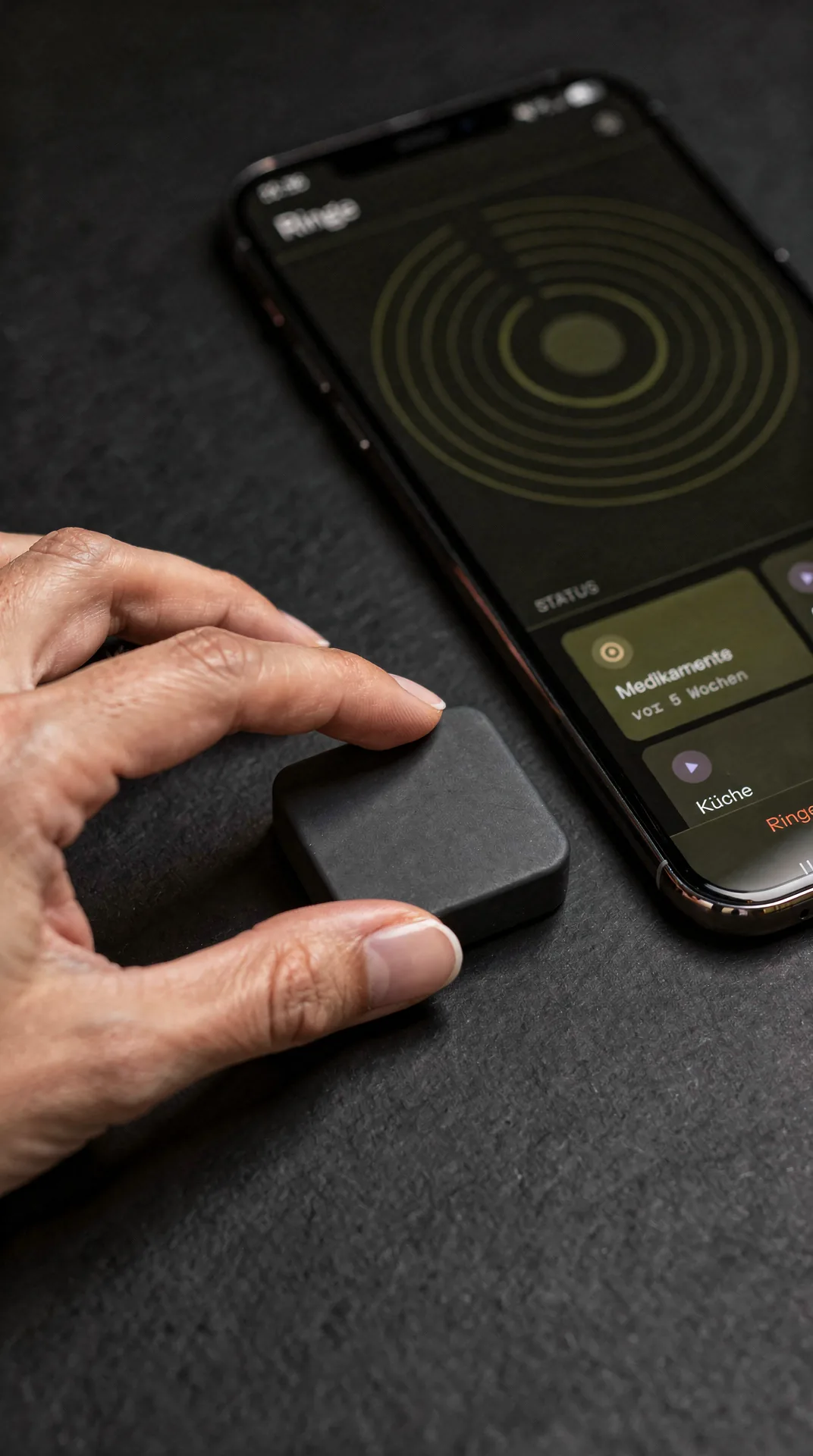 Nahaufnahme eines schwarzen NFC-Tags zwischen zwei Fingern, daneben das Telefon mit dem Ringe-Bildschirm.